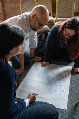 A group of people gathered around a big piece of paper on a table, discussing a workshop subject.