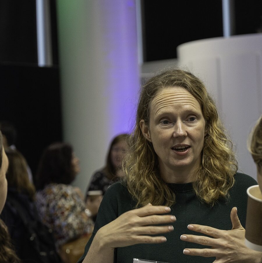 A cropped image of a woman talking to a few other women, gesticulating her hands while she is talking.