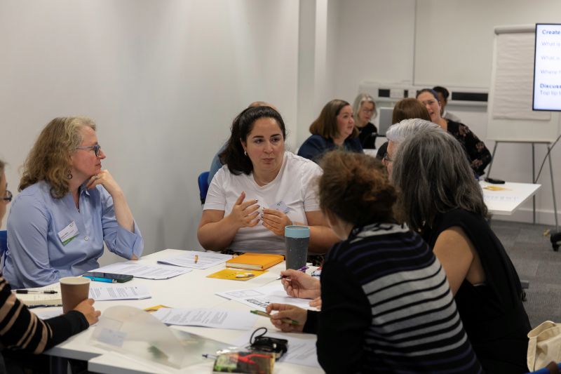 A group of women sit around a seminar table discussing a subject in a workshop.