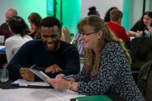 A man and a woman sat at a table discussing a topic on a piece of paper. Photograph from VitaeCon2023. 